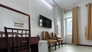 Un área de espera con un banco de madera, un televisor montado en la pared y una puerta que da al exterior.