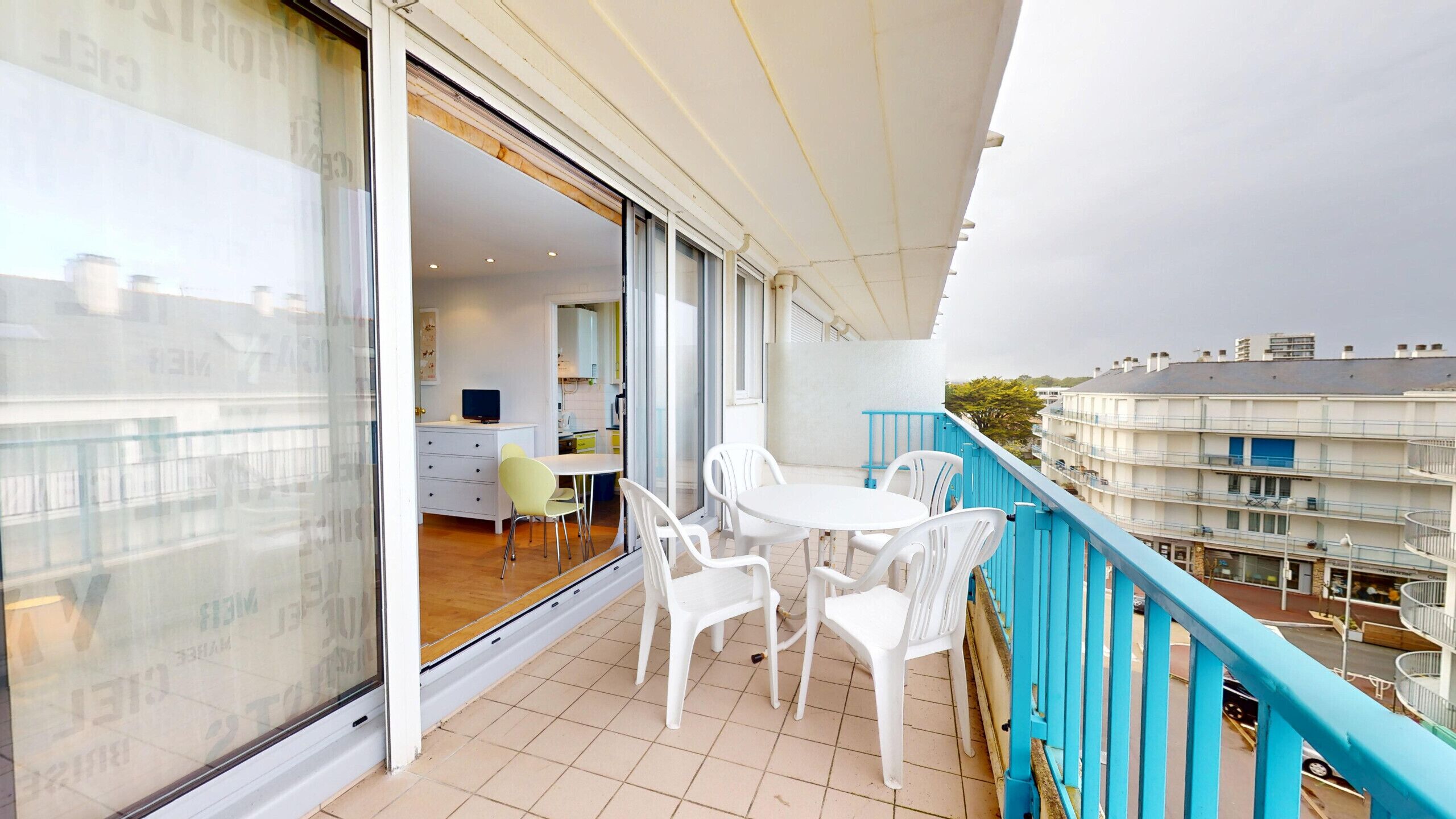 A balcony with a blue railing, white chairs, and a table.