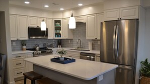 Una cocina moderna con gabinetes blancos, electrodomésticos de acero inoxidable y una isla central con taburetes.