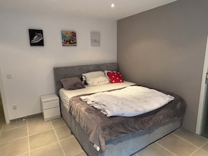 A bedroom with a bed, a nightstand, a wall-mounted shelf, and a door.