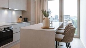 Een moderne keuken met een centraal eiland, een eetgedeelte met vier stoelen en een groot raam met uitzicht op de stad.