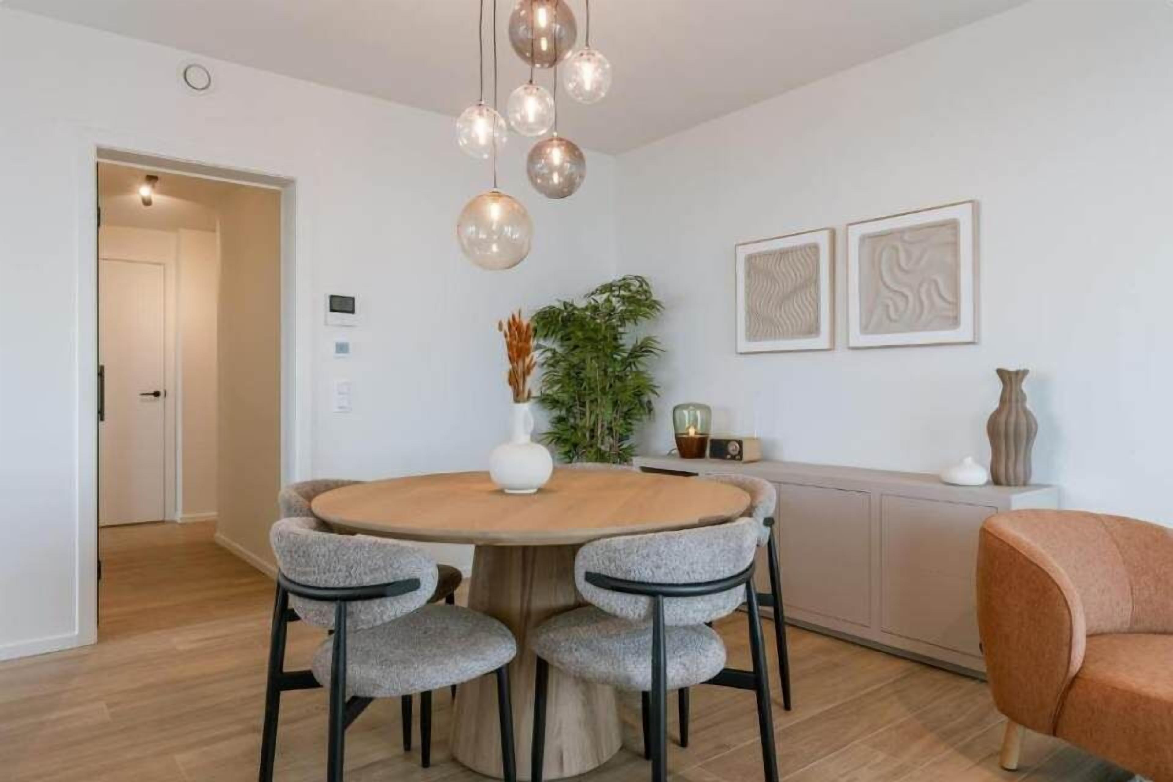 A dining area with a round table, four grey upholstered chairs, a wooden cabinet, and a potted plant.