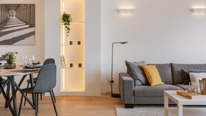 A modern living room with a grey sofa, a dining table with chairs, a bookshelf with plants, and a painting on the wall. - Trendy apartment close to the coast (Oostende)