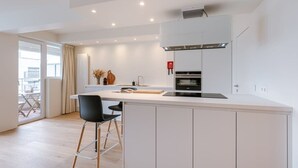 A modern kitchen with white cabinetry, a central island, and a black chair. - Trendy apartment close to the coast (Oostende)