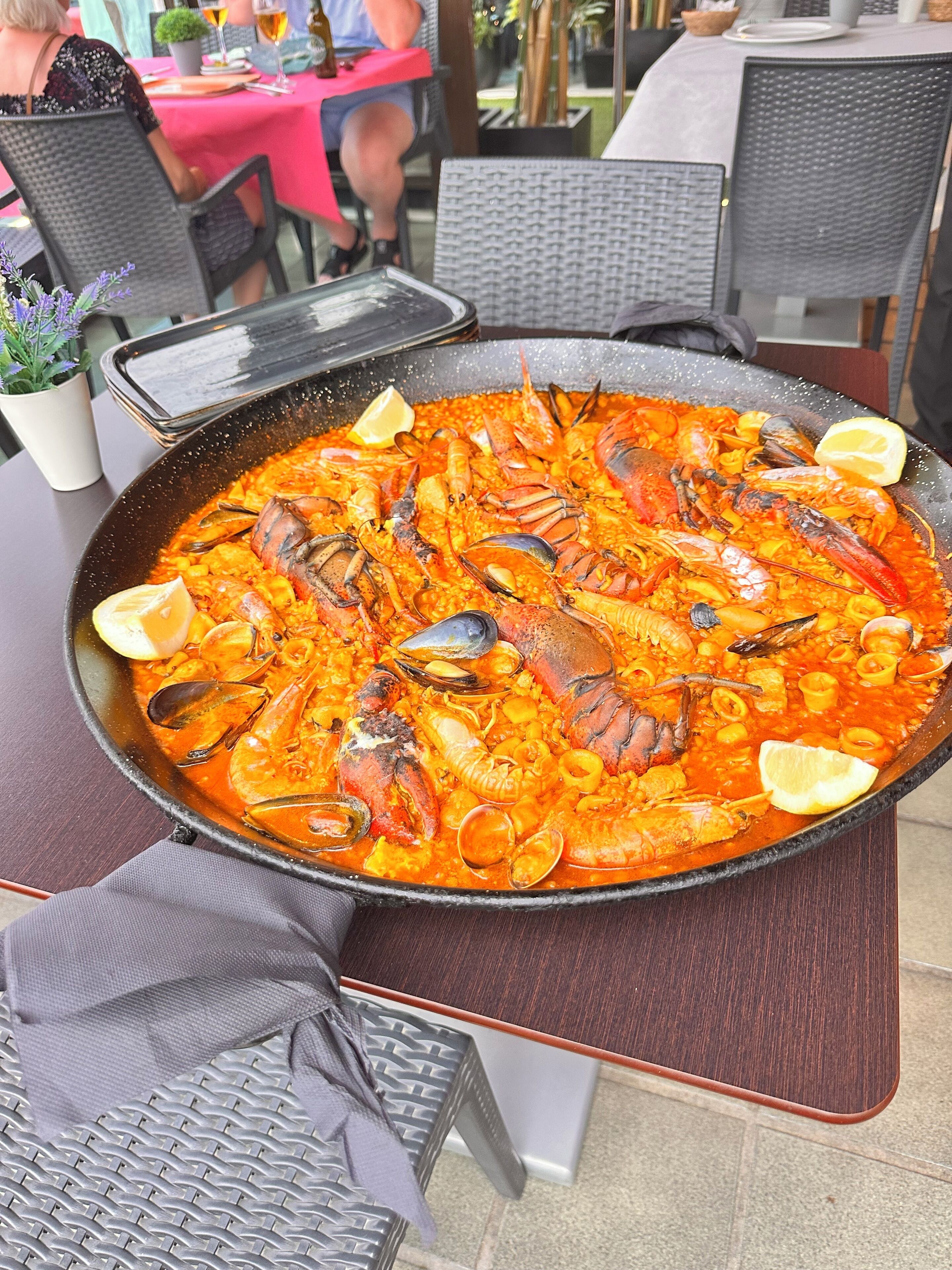 Eine große Paella mit Meeresfrüchten auf einem Tisch, um den herum Stühle stehen.