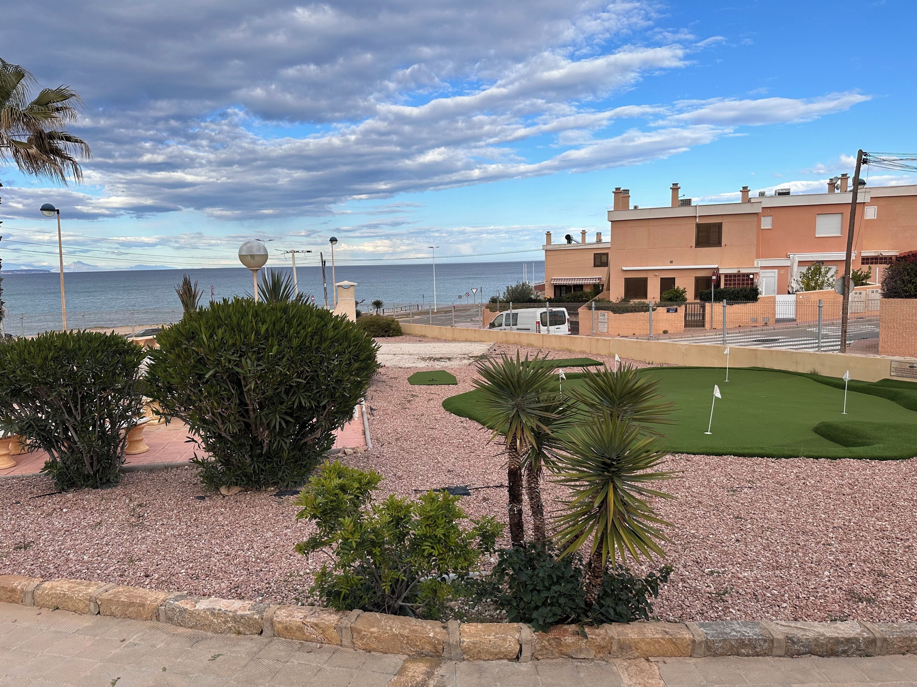 Vista costera con campo de golf, palmeras y un edificio con vista a la playa.