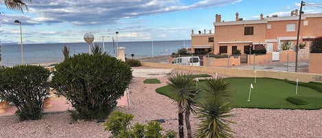 Vista costera con campo de golf, palmeras y un edificio con vista a la playa.