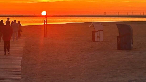 Eine Strandansicht mit Sonnenuntergang, einer Holzpromenade und einem Rettungsturm.