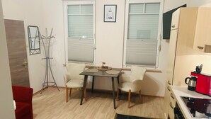 Ein gemütlicher Wohnbereich mit Esstisch, zwei Stühlen, einem roten Sofa, einer Küchenzeile inklusive Herd und Kaffeemaschine sowie einem Heizkörper.