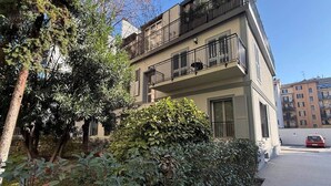 Un immeuble résidentiel à plusieurs étages, doté de balcons, d’un espace de stationnement et d’une voiture rouge garée sur le parking.