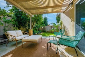 A covered patio with wicker furniture, a small table, and a green chair.