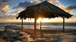 A beach scene with a thatched-roof structure, ocean waves, and a sunset. - Perfect for Families W/ Pool,Walk 2 Beach,Firepit! (San Diego)