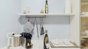 A kitchen with a white countertop, a coffee maker, a wine bottle, and a plate of fruit. - Listed 2-room apartment with historic Lindau ceiling (Lindau)