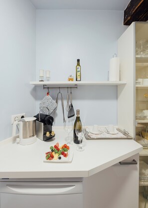 A kitchen with a white countertop, a coffee maker, a wine bottle, and a plate of fruit. - Listed 2-room apartment with historic Lindau ceiling (Lindau)