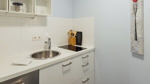 A modern kitchen with white cabinets, a stainless steel sink, and a black countertop. There is a wooden utensil holder and a small shelf with a glass container. - Listed 2-room apartment with historic Lindau ceiling (Lindau)