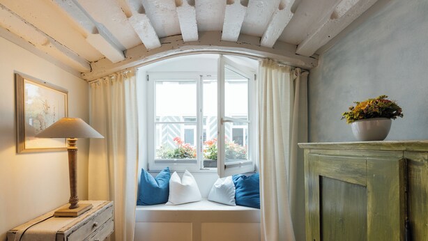 A room with a bay window, a wooden cabinet, a lamp, and a framed picture on the wall. - Listed 2-room apartment with historic Lindau ceiling (Lindau)