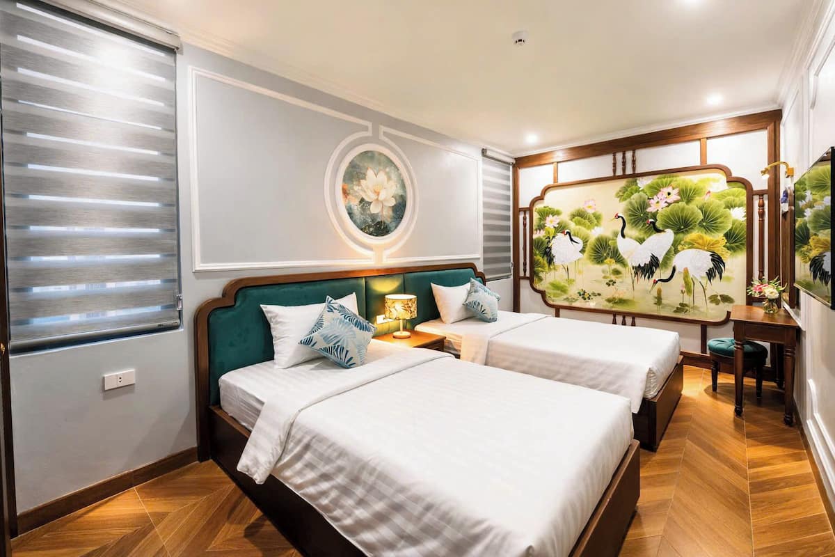Una habitación de hotel con cama, mesitas de noche, un escritorio y un cuadro grande en la pared.
