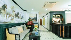 A reception area with a sofa, a coffee table, a painting of horses, a reception desk, and a clock. - OCEAN HOTEL NINH BINH (Hoa Lu)