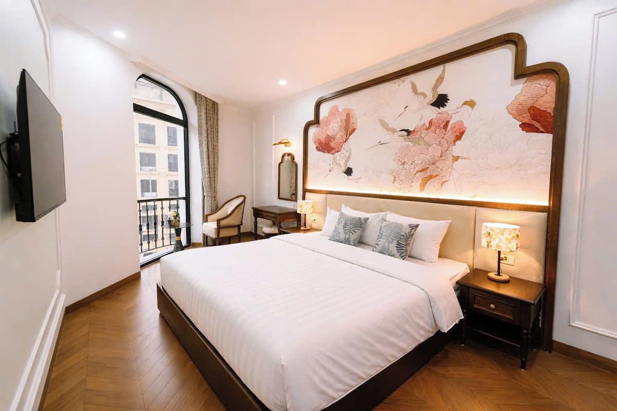 Una habitación de hotel con una cama grande, un escritorio, una silla, un televisor y una obra de arte floral de gran tamaño en la pared.