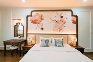 A bedroom with a large bed, two bedside tables with lamps, a nightstand, a chair, a desk, and a large floral artwork on the wall. - OCEAN HOTEL NINH BINH (Ninh Bình)