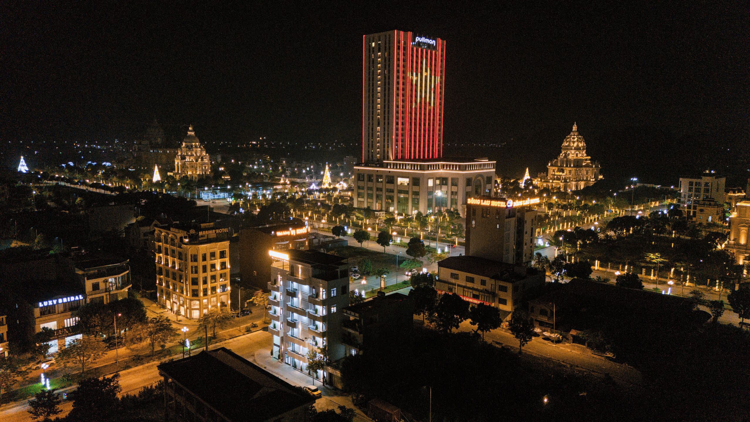 A cityscape at night with illuminated buildings, including a prominent hotel with vertical stripes.