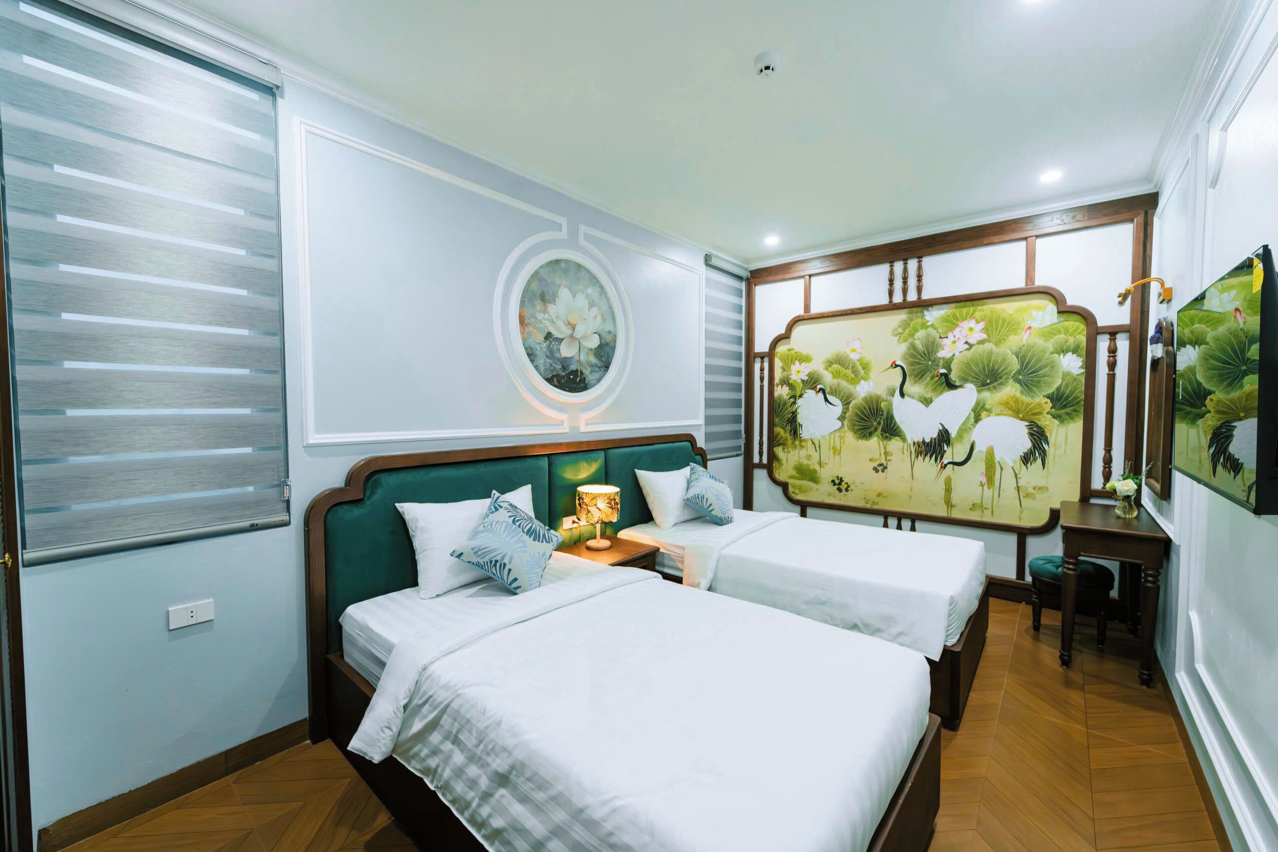 A hotel room with two beds, a nightstand, a wall-mounted TV, and a decorative screen with nature-themed artwork.