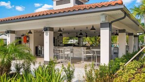 En udendørs patio med overdækket siddeområde, et køkken og en trappe op til en etage.