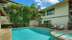 A swimming pool with a wooden deck, surrounded by lush greenery and a white fence.