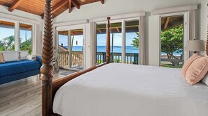 A bedroom with a large bed, a wooden ceiling, and a view of the ocean.