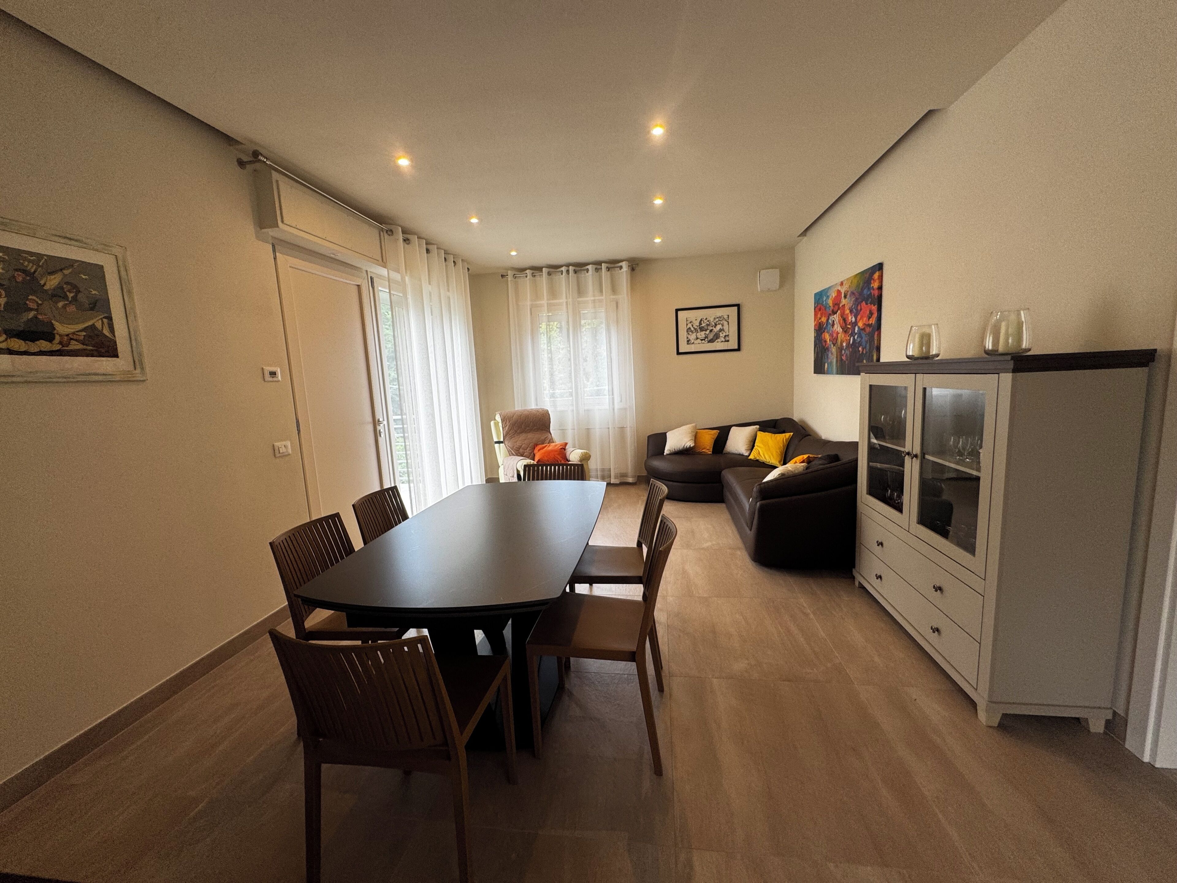 Ein Essbereich mit einem langen Tisch und Stühlen, einer Couch, einem Schrank mit Glastüren und einem Bild an der Wand.