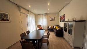 Un espace repas comprenant une longue table et des chaises, un canapé, un meuble avec des portes en verre et un tableau accroché au mur.