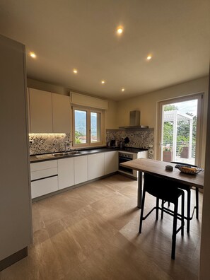 A modern kitchen with a dining area, large windows, and a view of the outdoors.