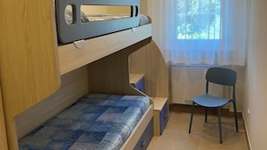 Un lit superposé avec un bureau et une chaise, une fenêtre avec des rideaux et un sol carrelé.