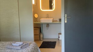 Et moderne hotelværelse med en pænt redt seng, et badeværelse med spejl og håndvask, og en dør der fører til et andet værelse.