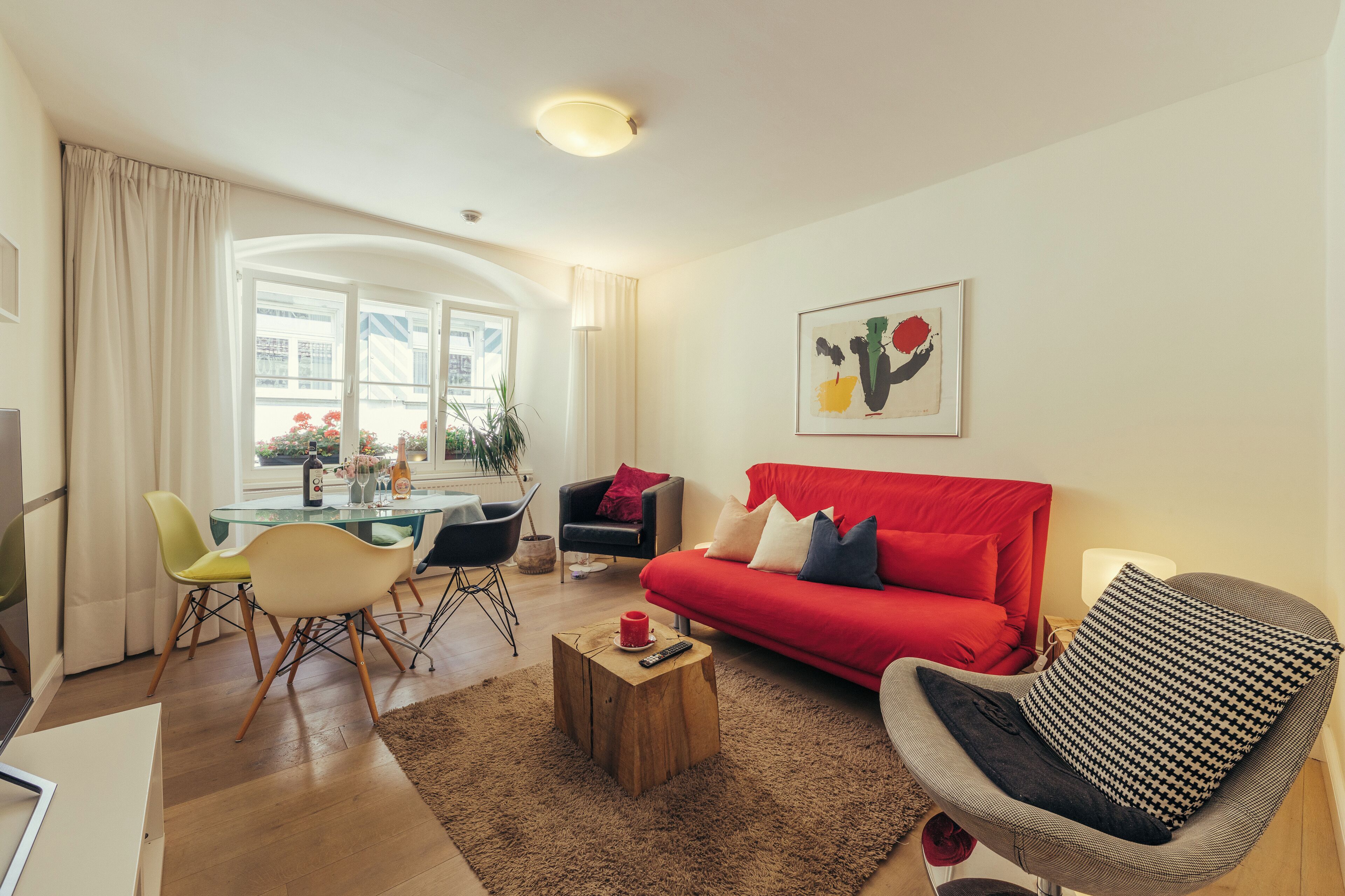 Un salon avec un canapé rouge, une table basse en verre et un fauteuil moderne. On y trouve également un coin repas avec une table et des chaises en verre.