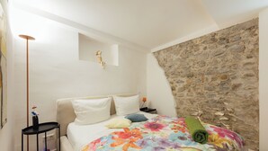 Une chambre à coucher avec un lit, une table de chevet, une lampe et un mur en pierre.