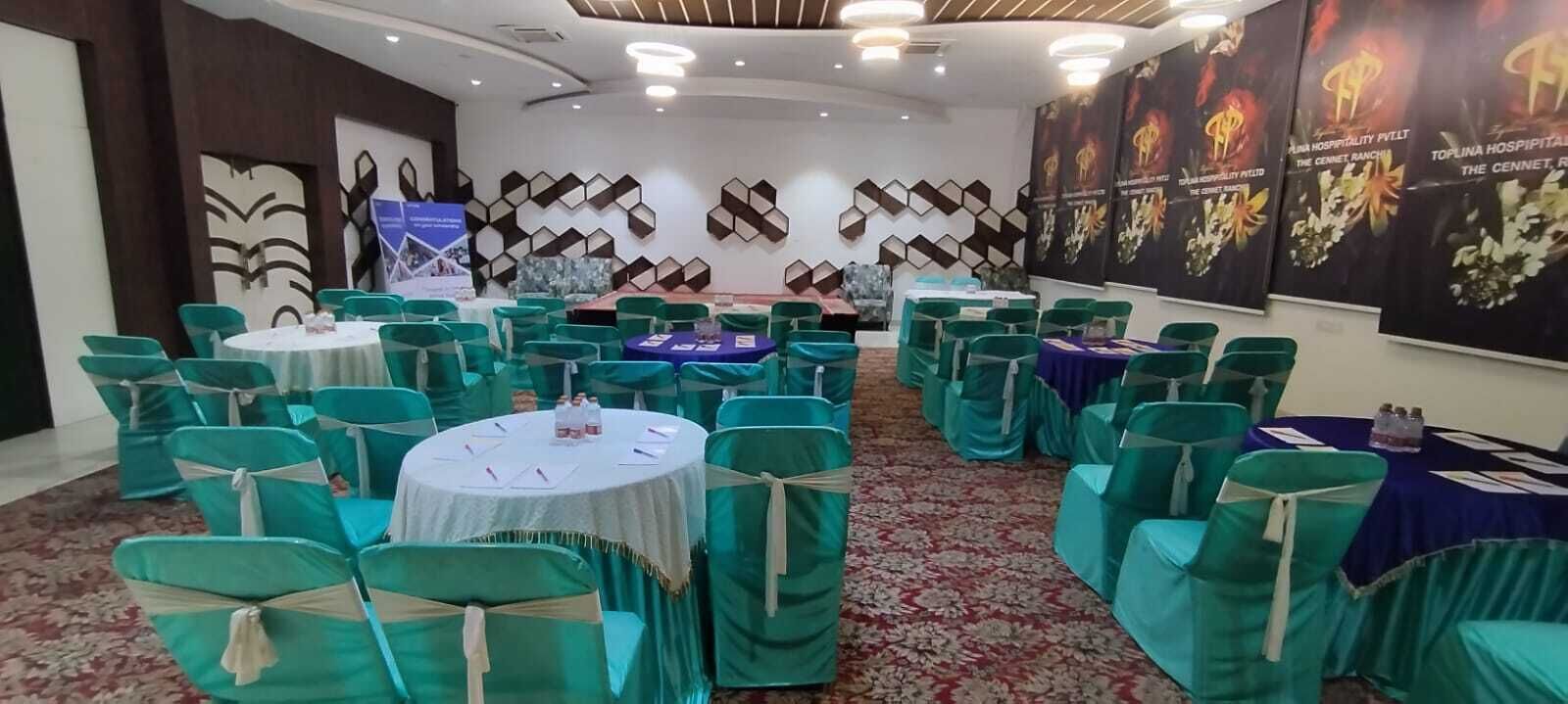 A conference room with round tables, green chairs, and floral carpet.