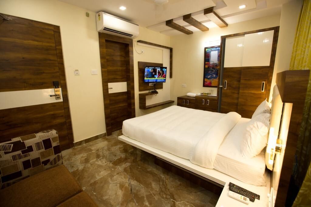 A hotel room with a large bed, a TV mounted on the wall, a wardrobe, and a small seating area.