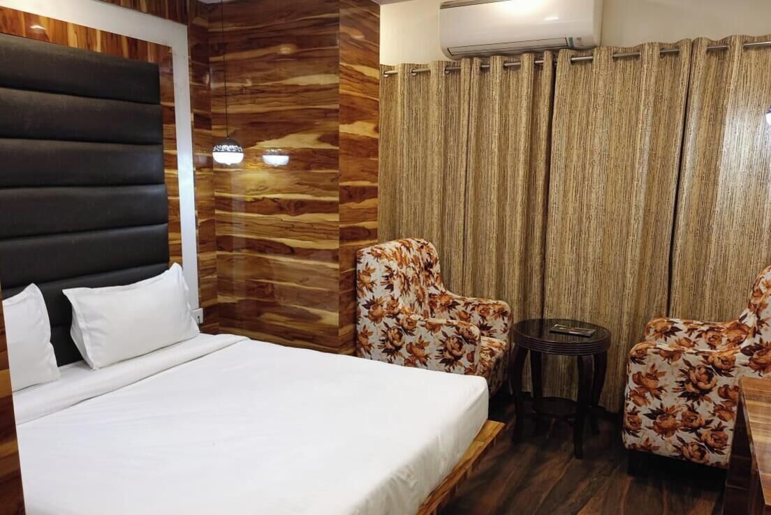 A hotel room with a large bed, two floral armchairs, a small round table, and a wooden accent wall.