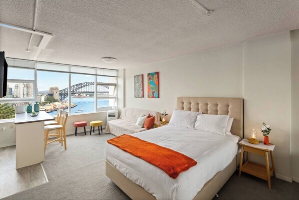 Et moderne hotelværelse med en stor seng, et skrivebord og udsigt til Sydney Harbour Bridge.