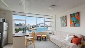 Een modern appartement met een keuken, eetgedeelte en woonkamer. Het heeft grote ramen met uitzicht op de Sydney Harbour Bridge en de skyline.