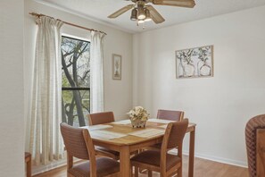 Comedor con mesa de madera, cuatro sillas, ventilador de techo y ventana con cortinas.