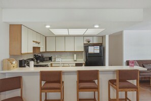 Eine moderne Küche mit weißen Schränken, einem schwarzen Kühlschrank und einer Bar mit vier Korbstühlen.