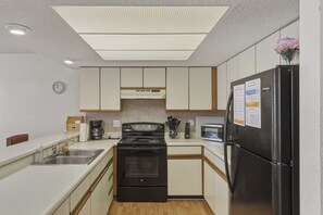 Una cocina compacta con estufa, lavamanos, refrigerador y un reloj en la pared.