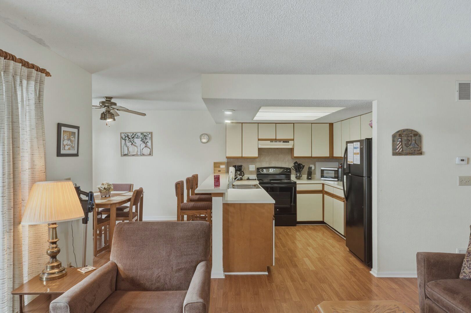 A modern kitchen with a central island, dining area with chairs, and a living room with a sofa.