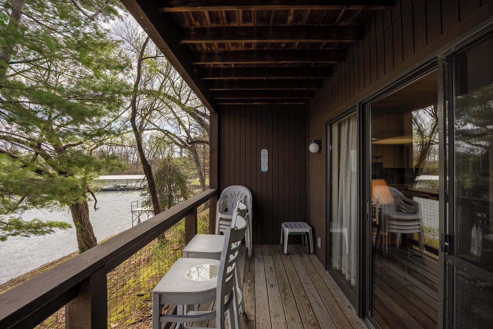 A wooden deck with a table and chairs, overlooking a body of water and trees.