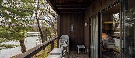 A wooden deck with a table and chairs, overlooking a body of water and trees.