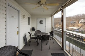 Een overdekt balkon met een tafel en stoelen, een plafondventilator en uitzicht op een steiger met boten.