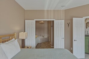Ein Schlafzimmer mit Bett, Nachttischlampe, einem Badezimmer mit Badewanne und einer Tür zu einem anderen Raum.