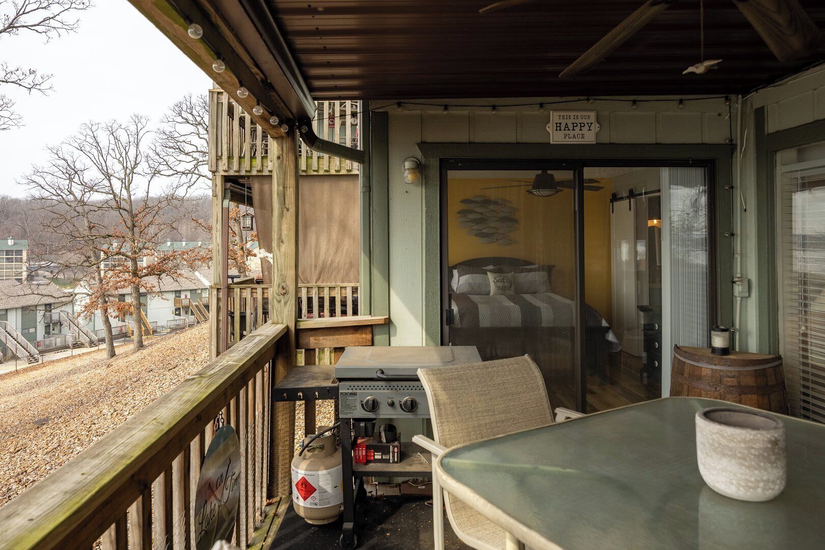 A balcony with a grill, a table, and a chair, overlooking a residential area.